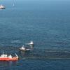 Group of vessels and a boom attempting to clean up spilled oil from the surface of the ocean