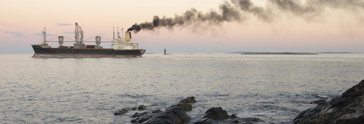 Ship in the middle of the ocean in front of a sunset with smoke billowing out