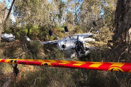 crashed light plane among trees and grass with red and yellow tape in the foreground