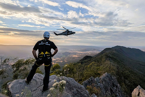 search and rescue officer from behind looking at helicopter over scenic mountain and valleys