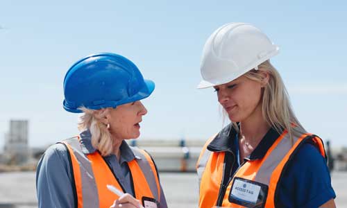 2 women on a ship dock in hard hats and orange vests