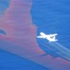 Aeroplane flying over an oil slick spraying dispersant