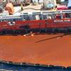 Ship with a boom attempting to recover the rust-coloured oil captured on the surface of the water