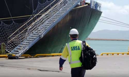 Man with hard hat, backpack and 'AMSA' high visibility vest viewed from behind walking towards ship