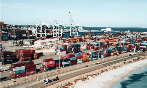 View of Port Kembla with cranes, containers, trucks and a beach in the foreground