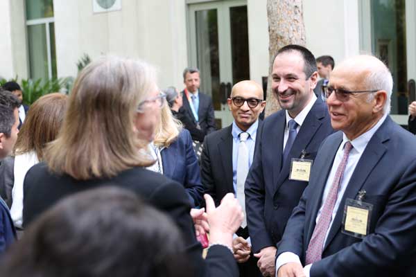 Men in suits smiling in courtyard with back of woman talking to them