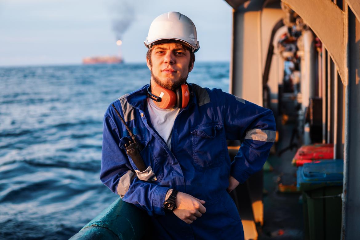 Image of seafarer on board a vessel, wearing a hardhat and ear muffs