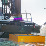 Commercial fisher wearing a lifejacket and safety gear hosing the deck