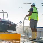 Fisherman wearing lifejacket and boots hosing deck
