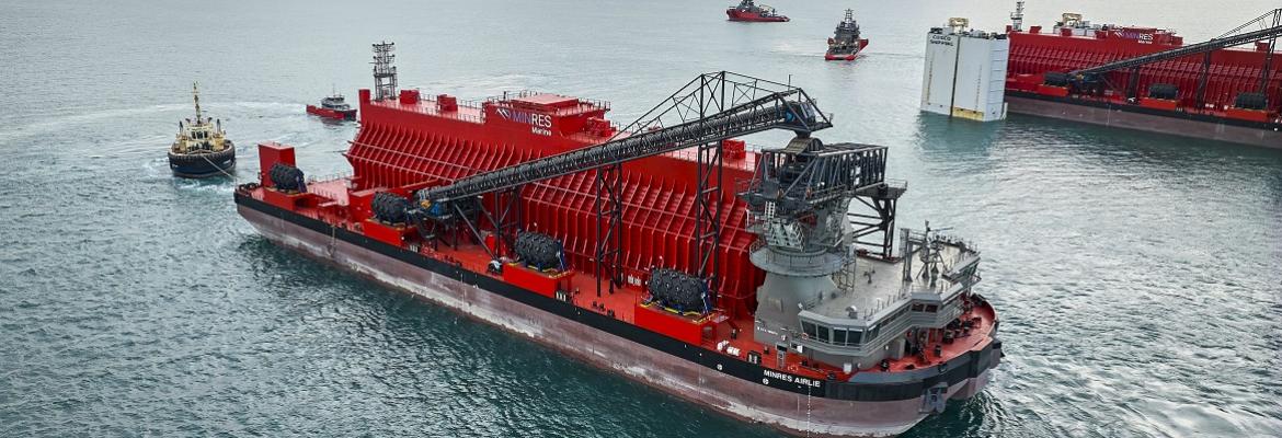 MinRes Airlie, a 123.8-metre transhipper and one of the two largest new domestic commercial vessels built in 2023–24, shown operating at sea. The red vessel features large onboard bulk handling infrastructure and is part of a matched pair with MinRes Coolibah.