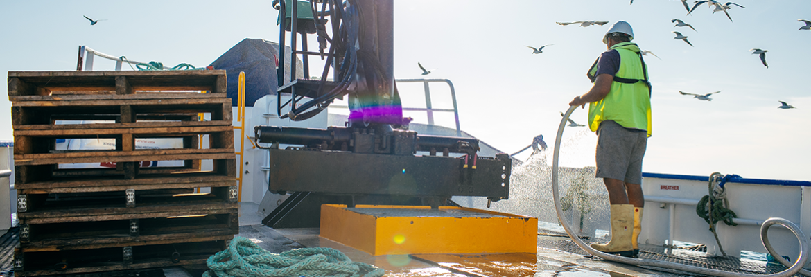 Commercial fisher wearing a lifejacket and safety gear hosing the deck