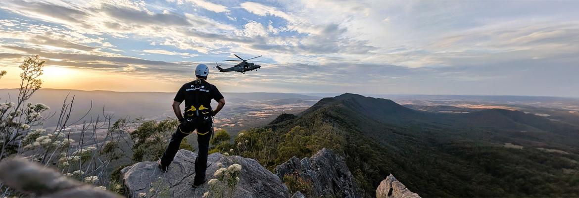 search and rescue officer from behind looking at helicopter over scenic mountain and valleys