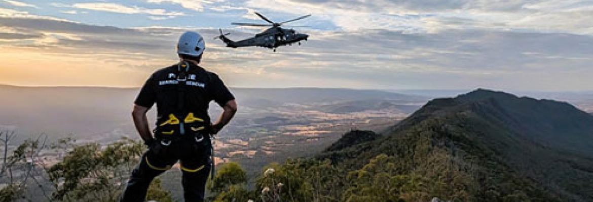 search and rescue officer from behind looking at helicopter over scenic mountain and valleys