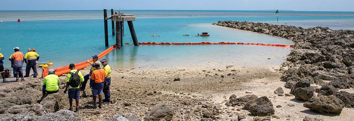 People looking out from the shore at Port Moresby and a containment boom