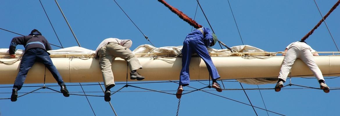 people hanging off a boom on a ship