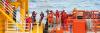 Workers in safety gear transfer between a vessel and offshore platform using a rope ladder, with ocean waves and safety equipment visible in the background.
