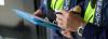 Close-up of two people wearing high-visibility vests and uniforms, holding pens and blue clipboards, with the word “Inspector” visible on their vests.